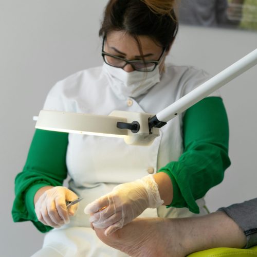 Concentrated skilled specialist wearing medical uniform doing procedure on leg of crop customer under light of lamp